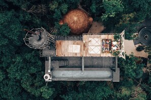 An aerial view of a rustic cabin with a wooden deck, a thatched roof, and a small outdoor seating area. - Ekumal Retreat Eco Sanctuary (Akumal)