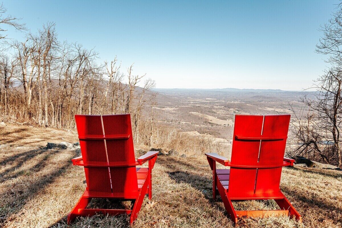 Twee rode stoelen met uitzicht op een glooiend landschap.