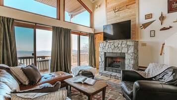 Un salón amplio con chimenea de piedra, sofás de cuero y un ventanal con vistas a una terraza.