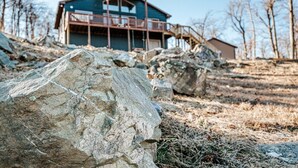 Eine Holzhütte mit Balkon, umgeben von großen Felsen und spärlicher Vegetation.