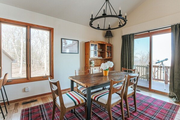 A dining area with a wooden table, chairs, a chandelier, and a view of the outdoors.