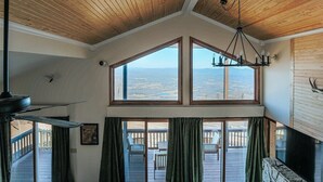 Ein Zimmer mit hoher Decke, großen Fenstern, einer Kristallleuchter und Blick ins Freie.