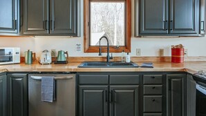 Eine Küche mit dunklen Schränken, einem Edelstahl-Kühlschrank, einer Mikrowelle, einem Toaster und einem Spülbecken mit Fenster darüber.