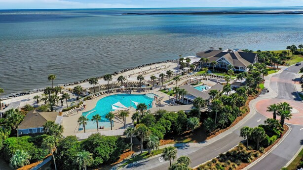 An aerial view of a resort with a large swimming pool, palm trees, and a beach area. - PERFECT 2BR Seabrook Getaway, Pool Access, Golf View, One Block to Beach & Club! (Seabrook Island)