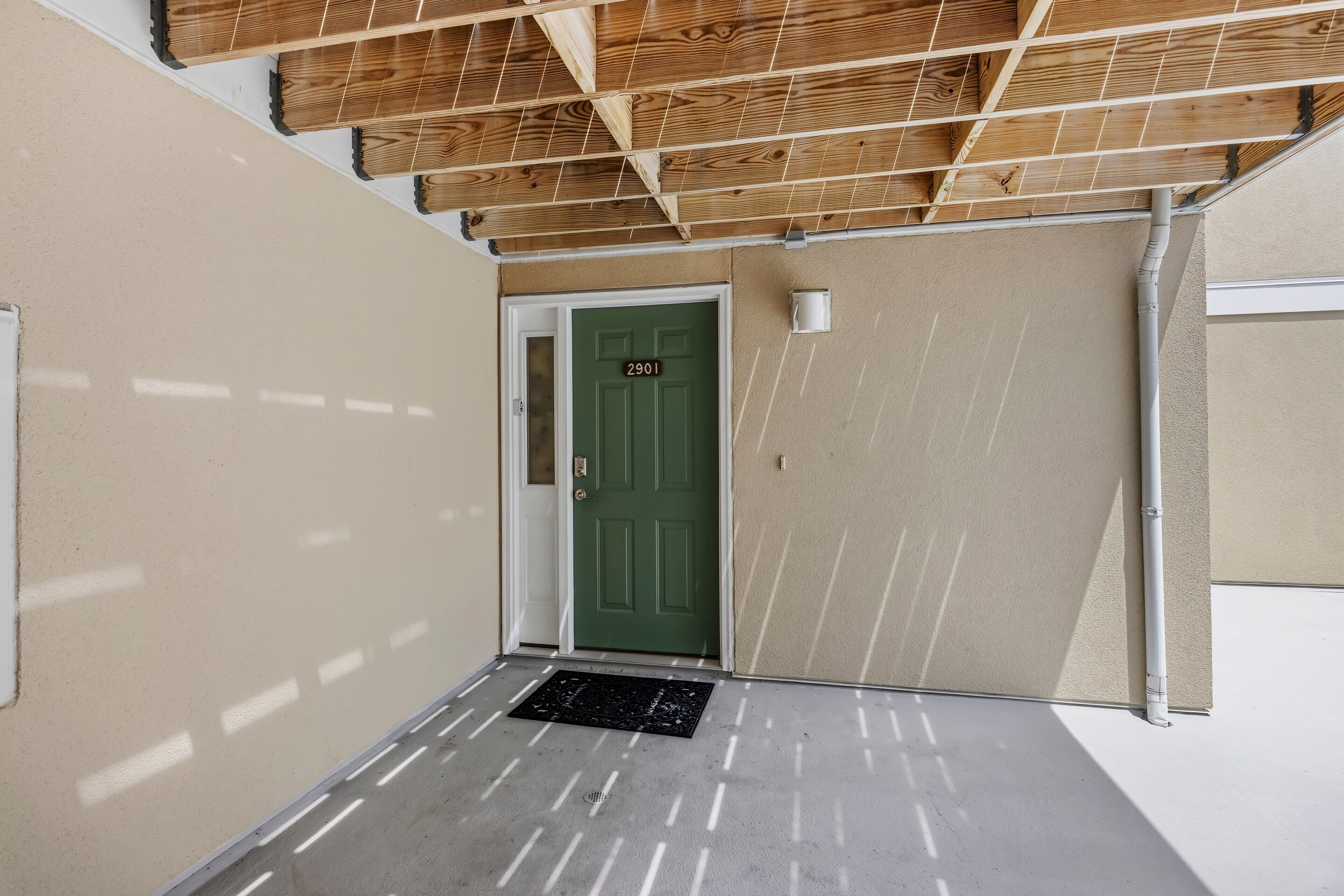 Entrada de un edificio con puerta verde, paredes color beige y techo de madera.