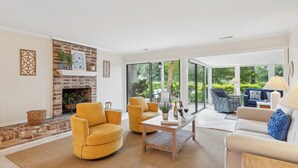 Een ruime woonkamer met een open haard, geel fauteuils, een salontafel en een bank.
