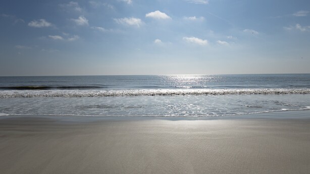 Een strand met een heldere lucht en zonlicht dat op het water schittert.