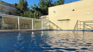 Una piscina con agua azul cristalina, rodeada por un muro color beige y una cerca de metal.
