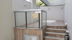 Un área de spa con cerramiento de vidrio, un jacuzzi y una escalera que conduce a una plataforma de madera.