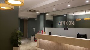 Un área de recepción con diseño moderno, que incluye un mostrador de recepción, un espejo grande y un letrero que dice "OPTION".