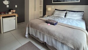Habitación de hotel con cama, mesita de noche y pequeño escritorio con refrigerador.