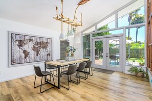 A dining area with a wooden table, four chairs, a world map artwork, a chandelier, and a view of the outdoors through large glass doors. - Surf House Cocoa Beach...Family-Friendly, Walk to Beach! (Cocoa Beach)