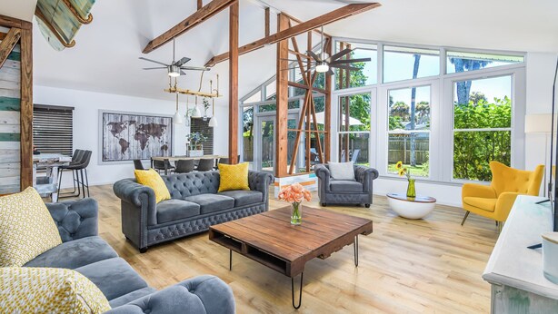 A spacious living room with a large window, a ceiling fan, and a coffee table. - Surf House Cocoa Beach...Family-Friendly, Walk to Beach! (Cocoa Beach)