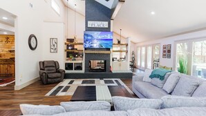 A spacious living room with a fireplace, a large flat-screen TV, a comfortable sofa, and a ceiling fan. - Peaceful Retreat near Texas Tech with Epic Game room! (Lubbock)