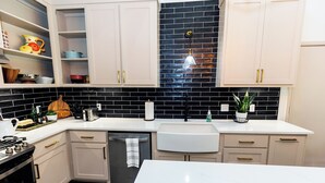 A modern kitchen with white cabinets, black and white backsplash, stainless steel appliances, and a white countertop. - Peaceful Retreat near Texas Tech with Epic Game room! (Lubbock)