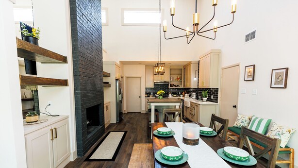 A modern kitchen with a fireplace, wooden flooring, and a dining area with a long table set for four. - Peaceful Retreat near Texas Tech with Epic Game room! (Lubbock)
