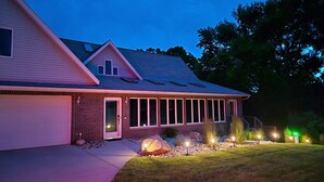 Uma casa de dois andares com garagem, varanda coberta e um jardim frontal ajardinado com iluminação decorativa.