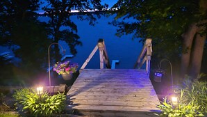 Une jetée en bois menant à une maison dont l’arrière-plan est illuminé de lumière bleue.
