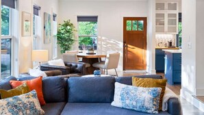 A modern living room with a dark blue sofa, a dining area with a wooden table, and a kitchen with blue cabinets.