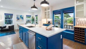 A modern kitchen with blue cabinets, a white countertop, and pendant lighting.