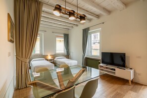 Quarto moderno com mesa de jantar de vidro, duas camas, uma TV e vista para a cidade.