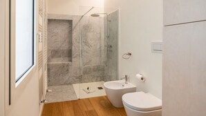 A modern bathroom with a glass-enclosed shower, a bidet, and a toilet.