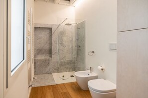 Um banheiro moderno com chuveiro de vidro, bidê e vaso sanitário.