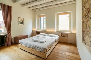 A bedroom with a wooden bed, two windows, a radiator, and a stone wall.