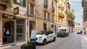 A cobblestone street with a white SUV parked on the side, a building with a sign reading 'DOPPIO MALTO,' and another building with a sign 'Biree, cucina e felicita.'