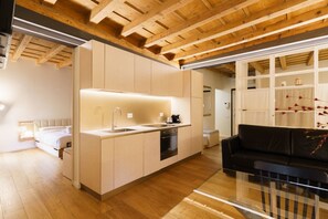 A modern kitchen with wooden beams, a black sofa, and a glass coffee table. - Modern residence with balconies overlooking Piazza Erbe (Verona)