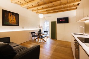 A modern kitchen with a wooden ceiling, a dining area with a table and chairs, a black sofa, and a framed painting on the wall. - Modern residence with balconies overlooking Piazza Erbe (Verona)