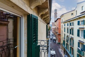 A narrow street with buildings on either side, a balcony with green shutters, and a clock tower in the distance. - Modern residence with balconies overlooking Piazza Erbe (Verona)