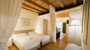 A hotel room with two beds, a wooden ceiling, a painting on the wall, and a lamp.