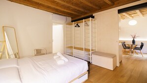 A bedroom with a large bed, a wooden ceiling, a walk-in closet, a mirror, and a dining area with chairs and a table.