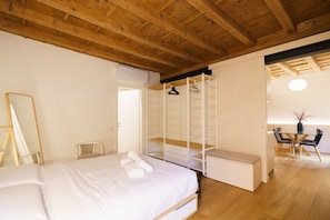 A bedroom with a large bed, a wooden ceiling, a walk-in closet, a mirror, and a dining area with chairs and a table. - Modern residence with balconies overlooking Piazza Erbe (Verona)