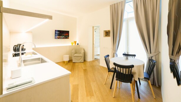 Cozinha moderna com pia, área de refeições com mesa e cadeiras, e sala de estar com sofá e televisão.