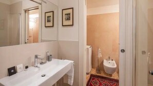 Un baño moderno con un espejo grande, dos cuadros enmarcados, un lavamanos blanco y un bidé.