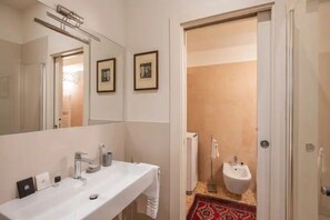 A modern bathroom with a large mirror, two framed pictures, a white sink, and a bidet.