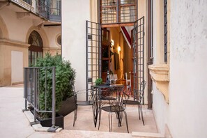 An outdoor seating area with a table and chairs, a potted plant, and a view of a building entrance.