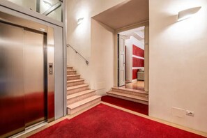 A hallway with a red carpet, an elevator, and a staircase leading to another room.