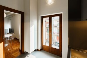 Una habitación con puerta de madera, zona de comedor con mesa y sillas, y vista a un balcón con barandillas.