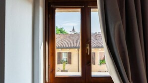 A wooden door with a glass panel, leading to a balcony with a tiled roof and a building with a pointed roof in the background. - Merici residence, elegant and fairytale-like (Verona)
