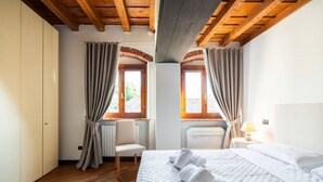 A bedroom with a bed, two windows with curtains, a chair, a bedside table with a lamp, and a radiator. - Merici residence, elegant and fairytale-like (Verona)