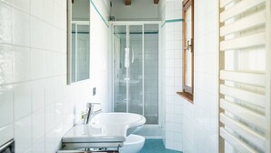 Un baño con azulejos blancos, una bañera blanca, cabina de ducha con mampara de vidrio y techo de madera.