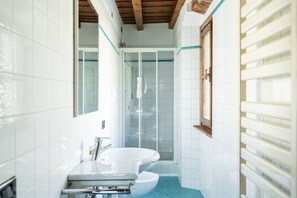 Un baño con azulejos blancos, una bañera blanca, cabina de ducha con mampara de vidrio y techo de madera.