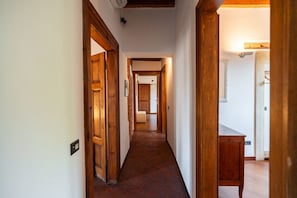 A narrow hallway with wooden doors and a tiled floor, leading to a room with a white wall and a small table. - Merici residence, elegant and fairytale-like (Verona)