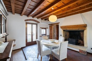 Un comedor con una mesa redonda, sillas blancas, una lámpara colgante y una chimenea.