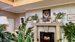 Un vaste salon agrémenté d’une cheminée, de grands pots de plantes et d’un haut plafond avec un balcon.