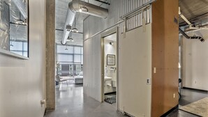 Un espace de bureau moderne au design épuré et industriel, caractérisé par des conduits apparents, une grande fenêtre et un espace toilettes bien visible.