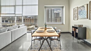 Un espace repas moderne avec une table en bois, des chaises noires et une vue sur la ville grâce à de grandes fenêtres.